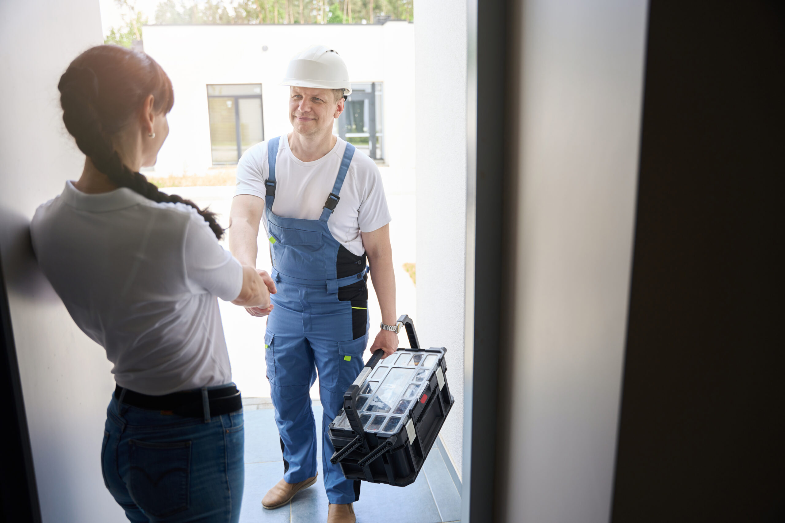 Woman and smiling adult caucasian repairman handshaking in entrance to new modern townhouse before repair in warm sunny day. Concept of work deal